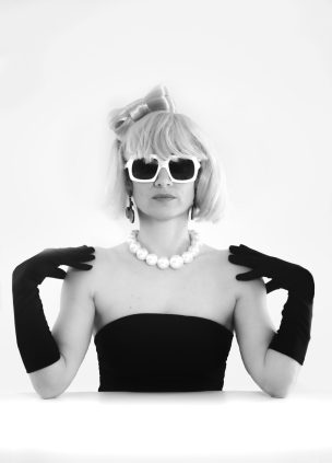 Femme au look rétro, portant des lunettes de soleil et des gants noirs, avec un collier.