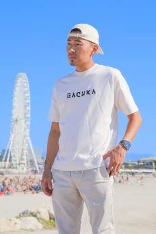 Homme en t-shirt blanc à la plage avec une grande roue en arrière-plan.