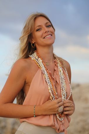 Femme souriante portant des colliers de perles sur fond de ciel nuageux.