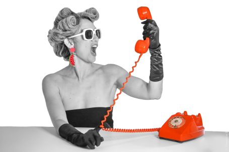 Femme glamour au téléphone vintage rouge, en lunettes de soleil et gants noirs.