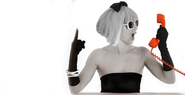 Femme au look rétro, portant des lunettes de soleil et un téléphone orange, exprime une émotion.