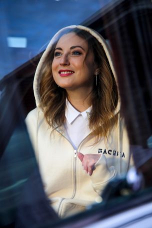 Femme souriante en sweat à capuche, assise dans une voiture.