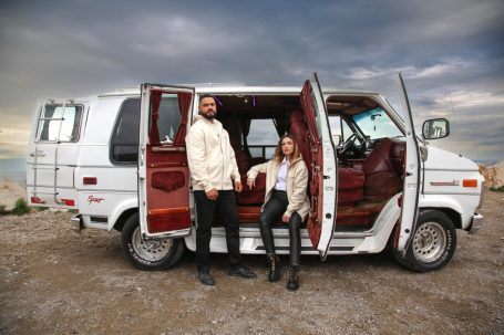 Un couple posant devant une fourgonnette blanche avec des portes arrière ouvertes.